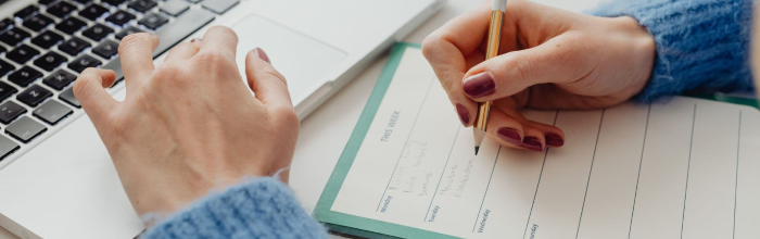 womans left hand on computer keyboard, right hand taking notes with pencil on paper