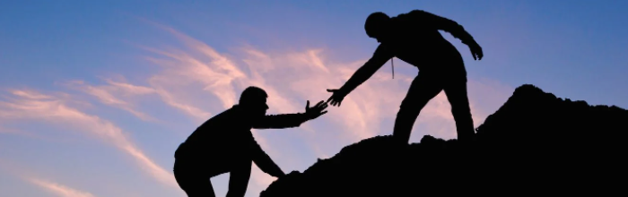 two men in shadow one reaching out to help the other up a mountain